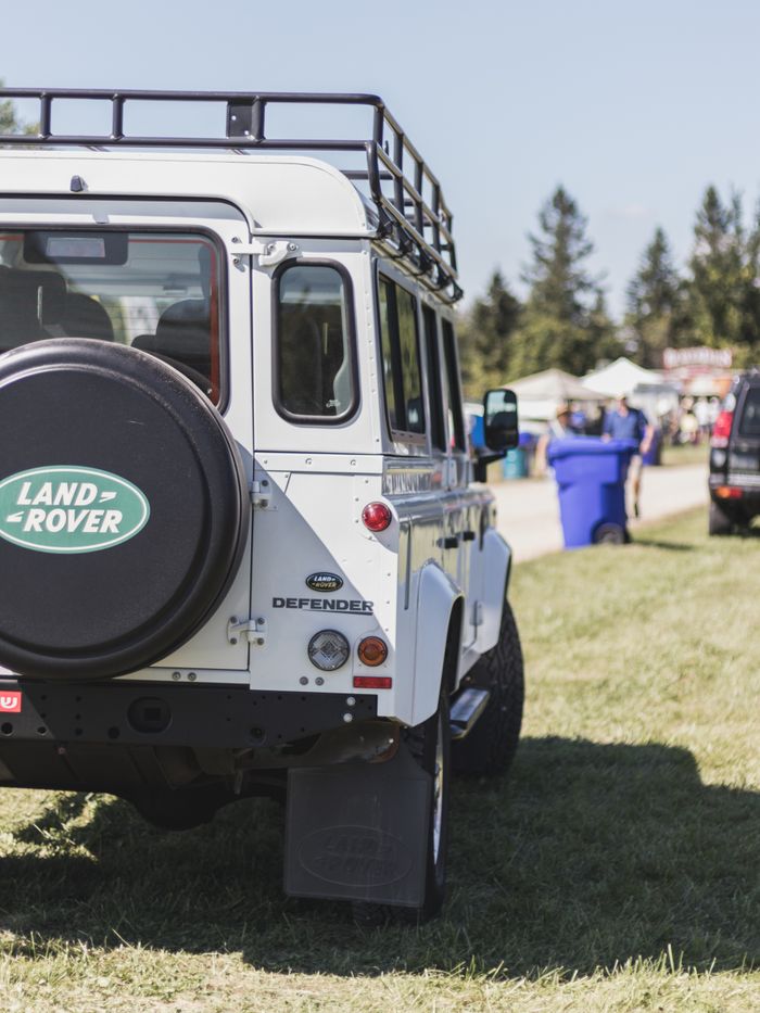 who-we-are Rear view of a classic white Land Rover Defender at an outdoor event, showcasing its iconic design.