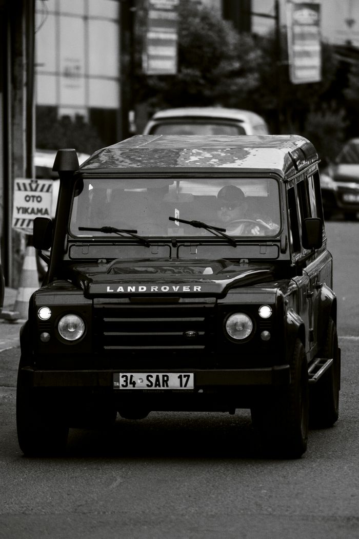 A vintage Land Rover drives through İstanbul's city streets, captured in a black and white photograph.