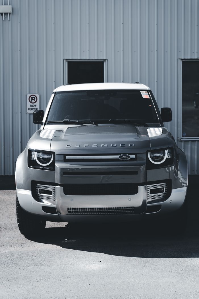 about-us Front view of a gray Land Rover Defender parked against an industrial wall.