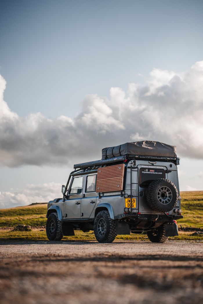 our-story A Land Rover Defender parked on a scenic route under dramatic clouds, perfect for adventure and travel themes.